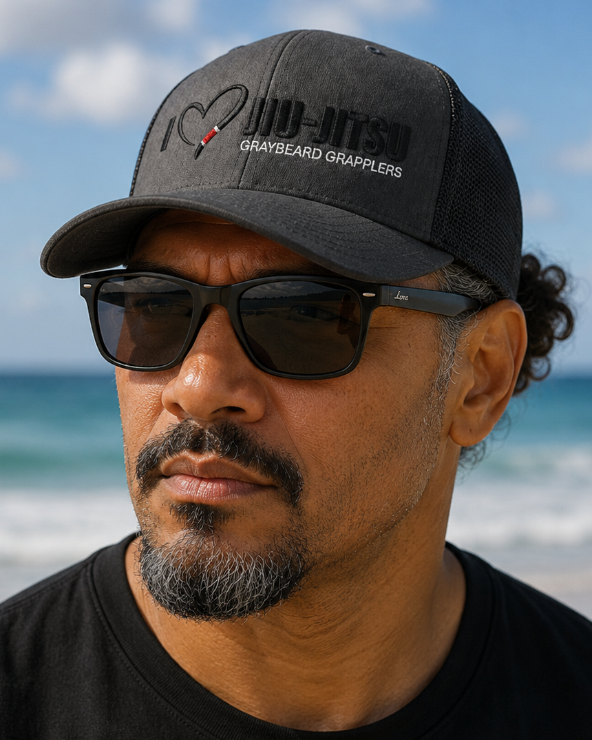 Man wearing a black cap and sunglasses on a beach with ocean and sky in the background