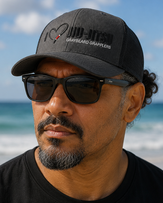 Man wearing a black cap and sunglasses on a beach with ocean and sky in the background